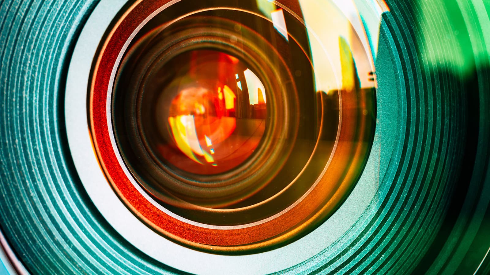 A close-up photo of a DSLR camera lens with green focus/zoom/aperture rings and orange light reflected in the glass.