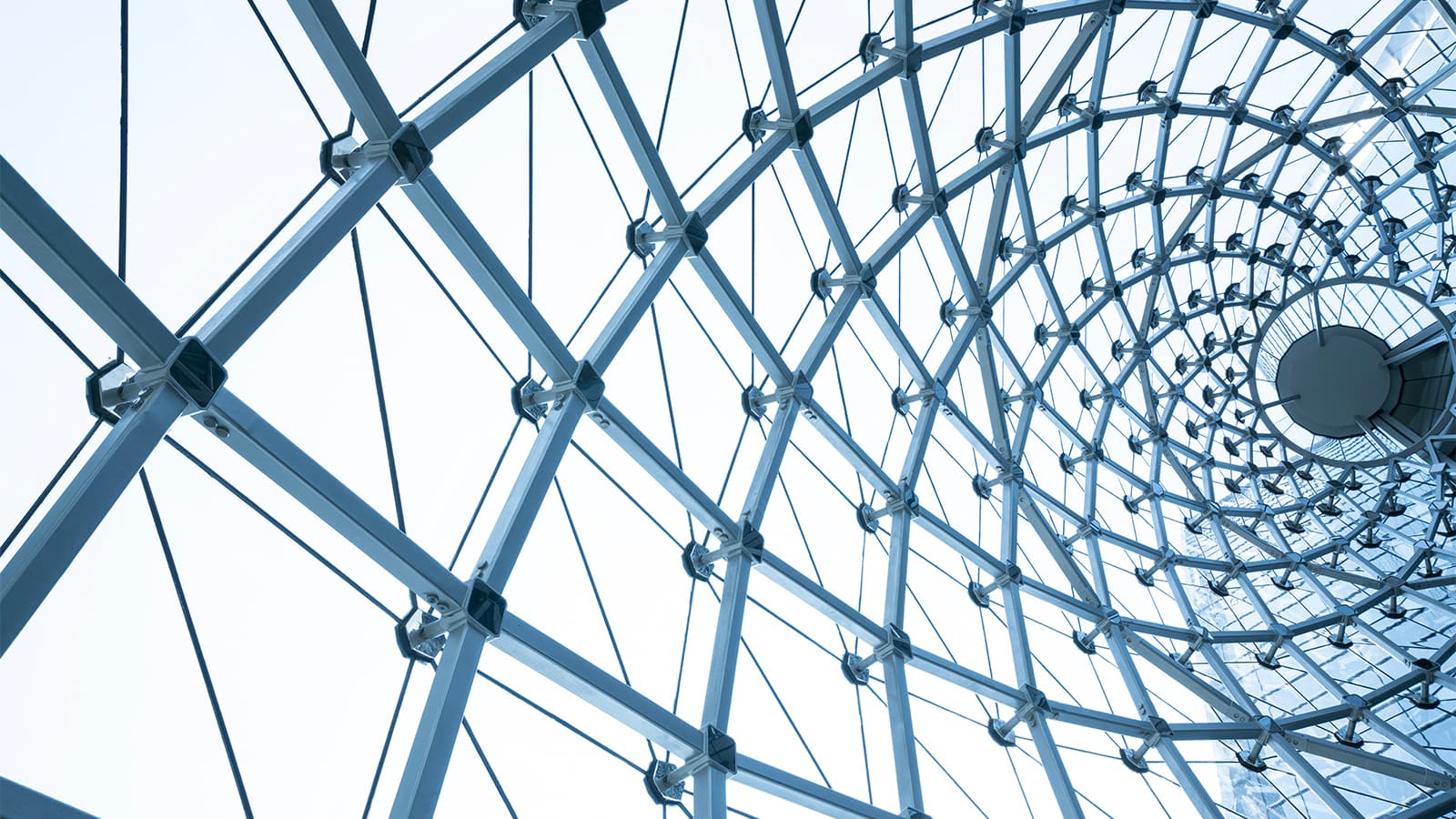 Close-up of a building with metal steel framework and glass, viewed from an interesting angle. Grey-blue framework with clear panels.